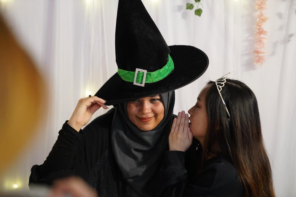 Fan wearing a witch hat while another guest helps adjust the look at the Wicked event. | TGV Blog