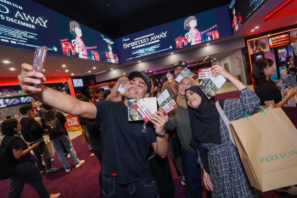 Fans taking a selfie at TGV during a Spirited Away fan event, holding event passes with the movie visuals displayed across the cinema foyer screens. | TGV Blog