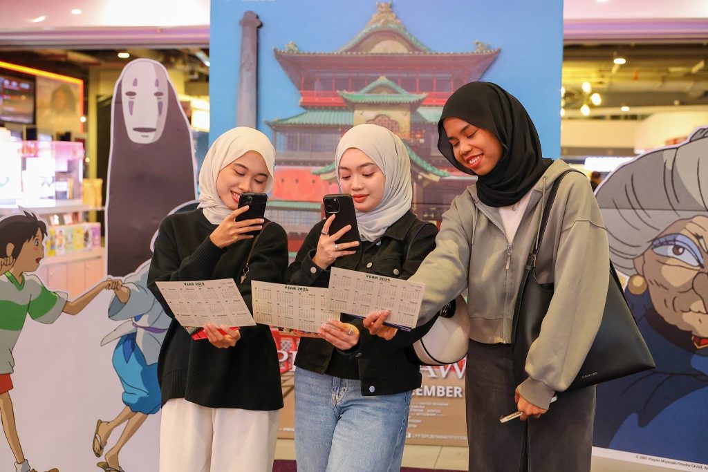 Fans reading and posing with their Spirited Away event passes in front of a themed photo wall at TGV. | TGV Blog