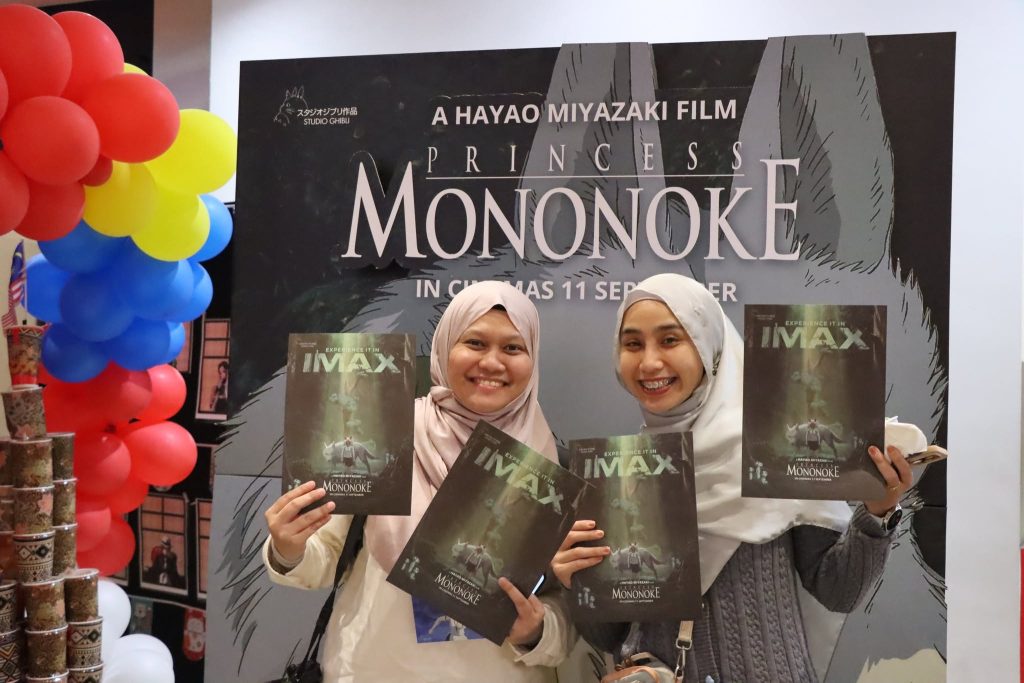 Two fans posing with Princess Mononoke posters in front of the event backdrop at TGV. | TGV Blog