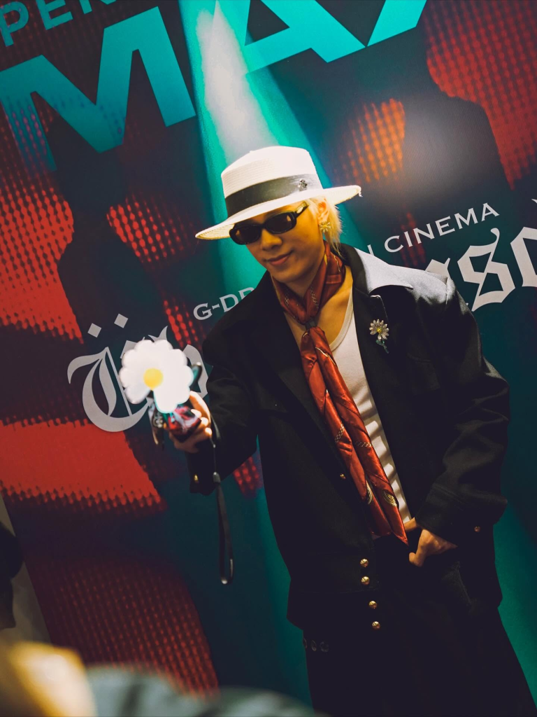 Fan dressed in a G-Dragon-inspired outfit holding a daisy prop at the GD Ubermensh event photo wall | TGV Blog